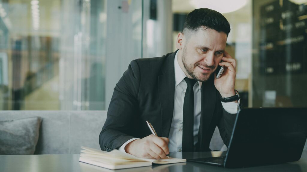 Professional man in suit multitasking with phone and laptop in modern office.